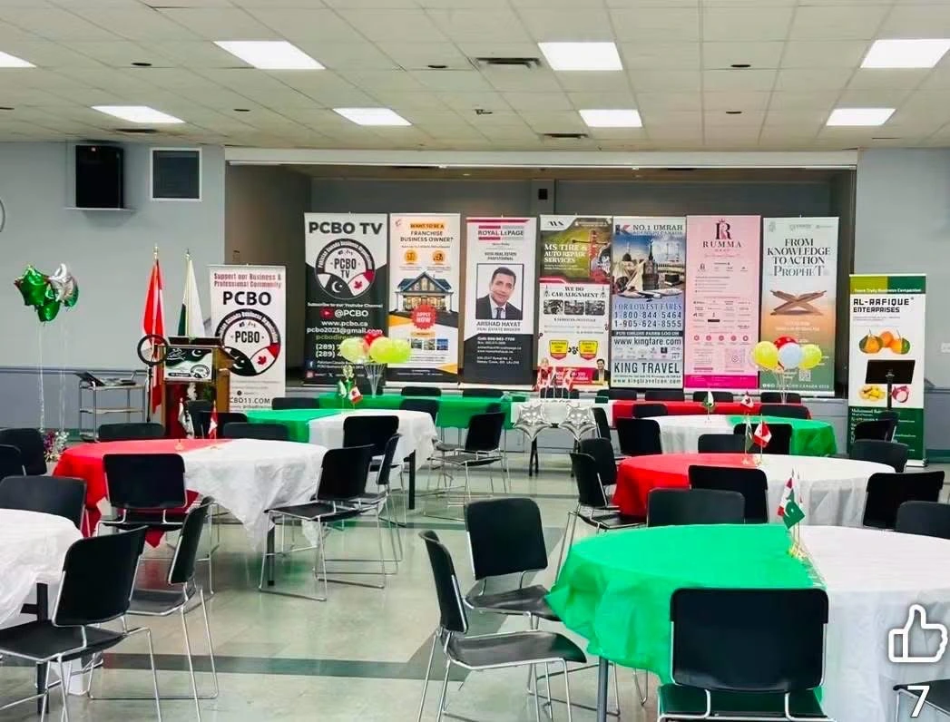 A wide view of an Independence Day hall setup with green, red and white tables and sponsor banners